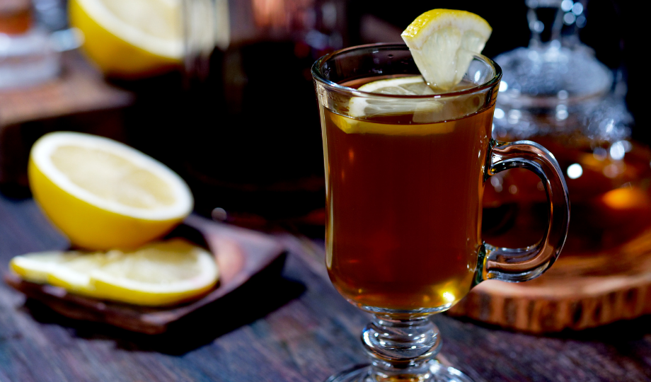 A hot toddy - a whiskey drink in a glass mug surrounded by lemon slices