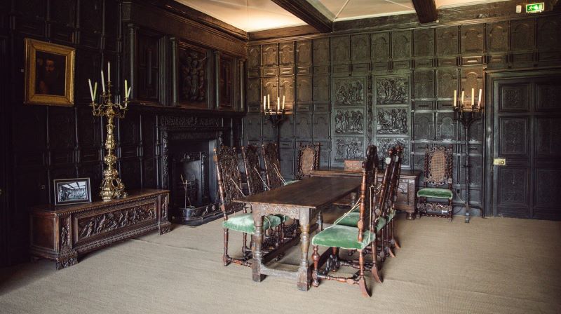 An interior of a castle showing an ornate table and chair set with dark panelled walls.