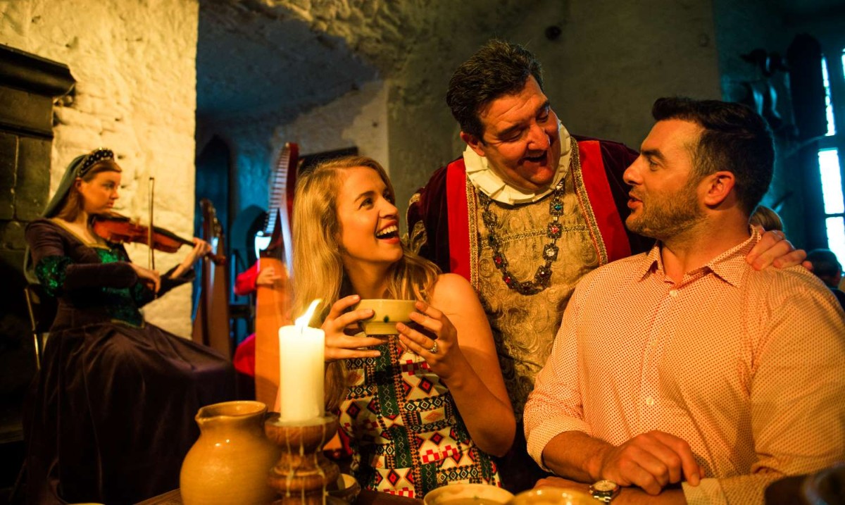 A costumed medieval lord talks to a couple in a genuine castle