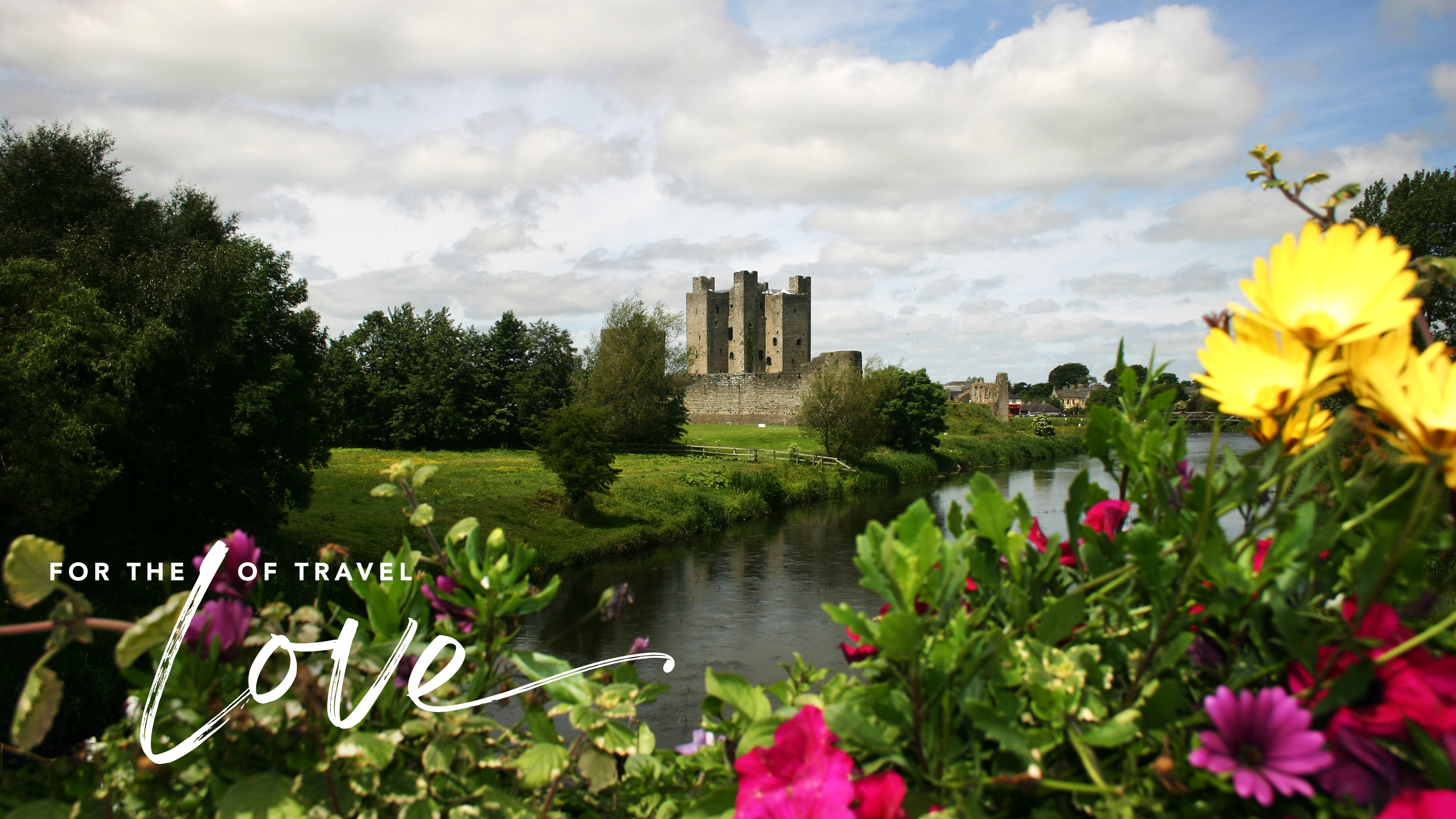 Lush garden with colorful flowers overlooking a river and historic stone ruins in the distance