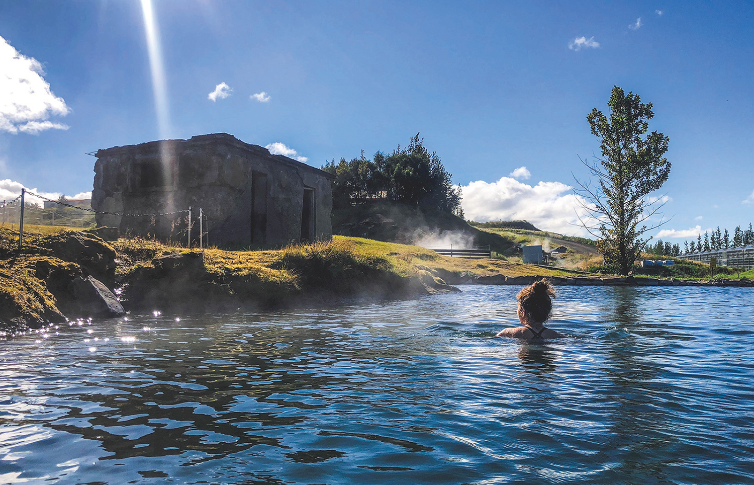 Woman swimming in the Secret Lagoon under a sunny sky