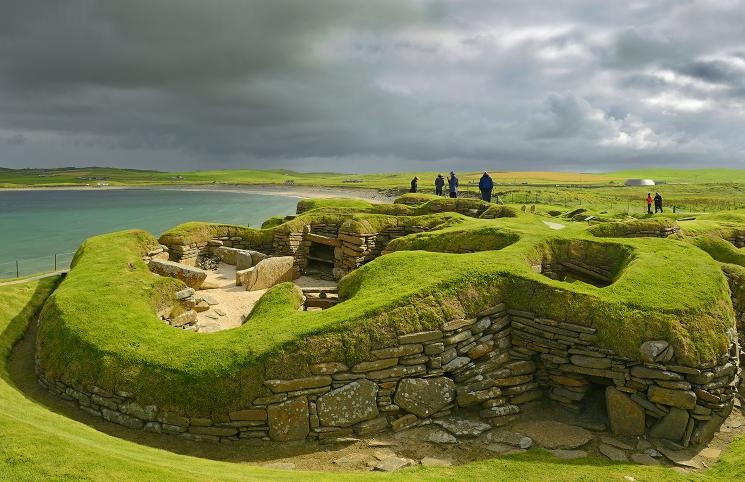 People walking among the grass-covered ruins of Skara Brae in Scotland